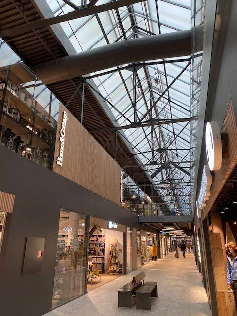 Lys og moderne handlegate i kjøpesenter med glasstak og synlige stålkonstruksjoner.