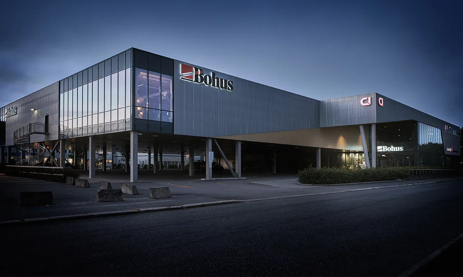 Stor butikkbygning i moderne stil med logoene Bohus og Schmidt, belyst på kveldstid.