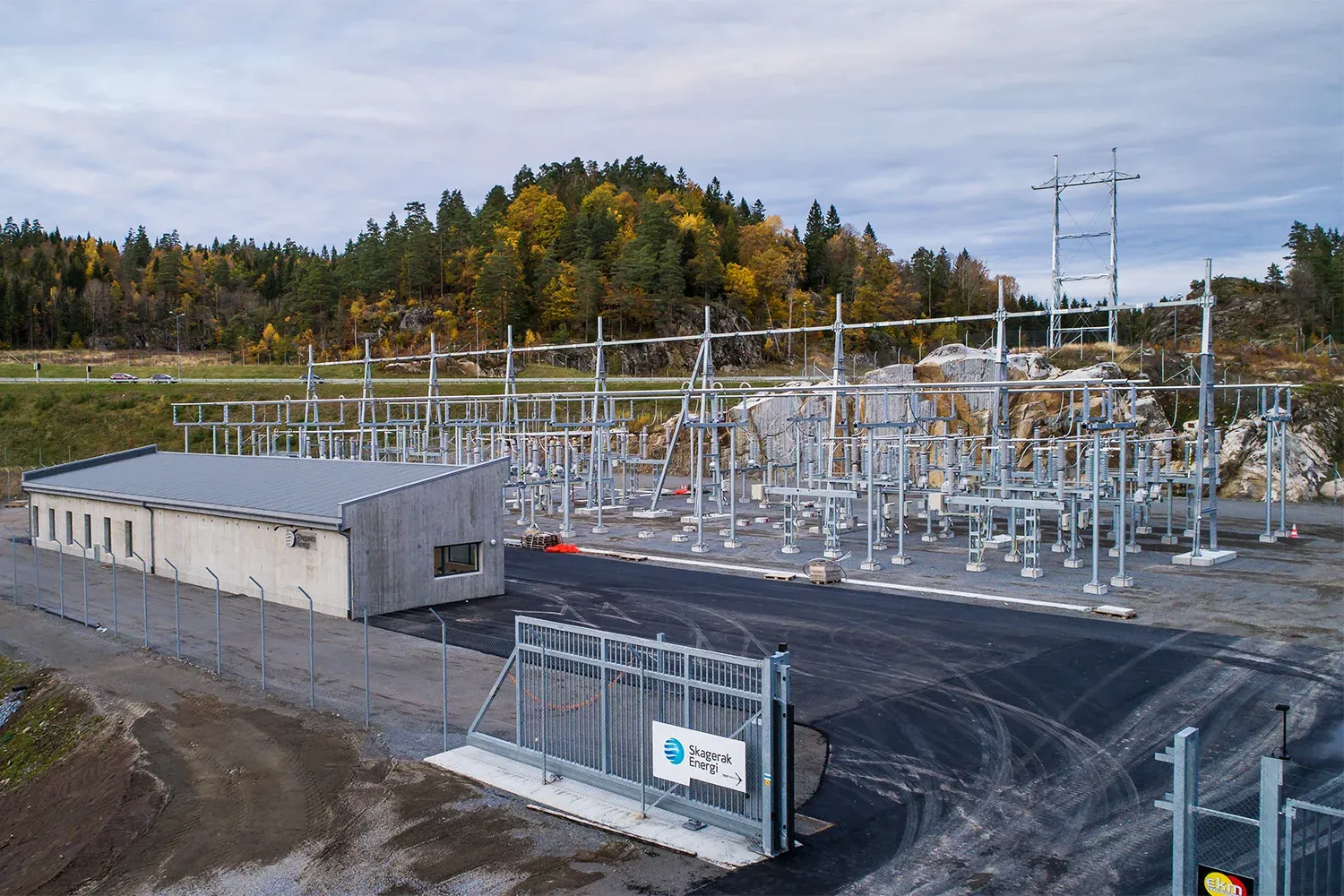 Inngjerdet transformatorstasjon med Skagerak Energi-logo, omgitt av høstfarger og fjellknauser.