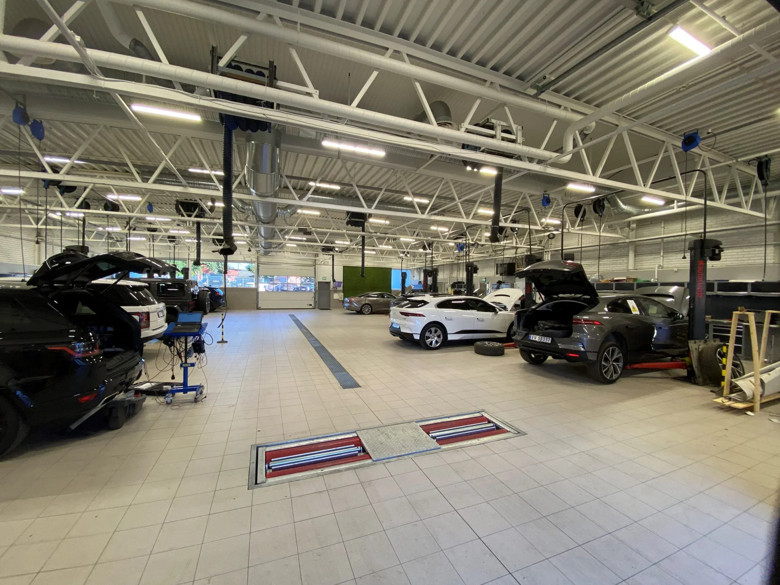 Stor verkstedhall med flere biler på løftebukker og moderne belysning under høyt tak.