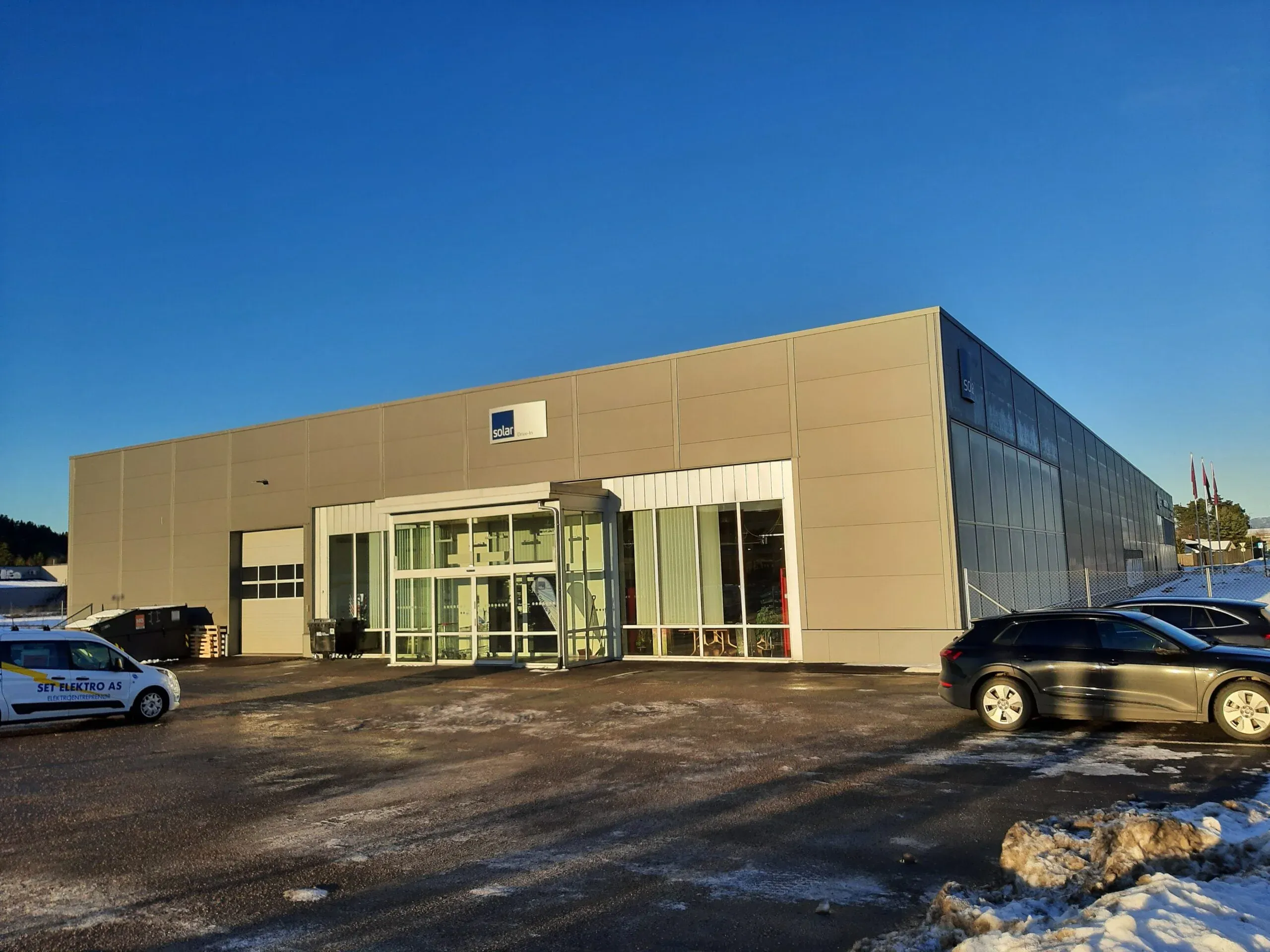 Bygning med skiltet "Solar" ved inngangsparti, omgitt av biler og snø på bakken under klar himmel.