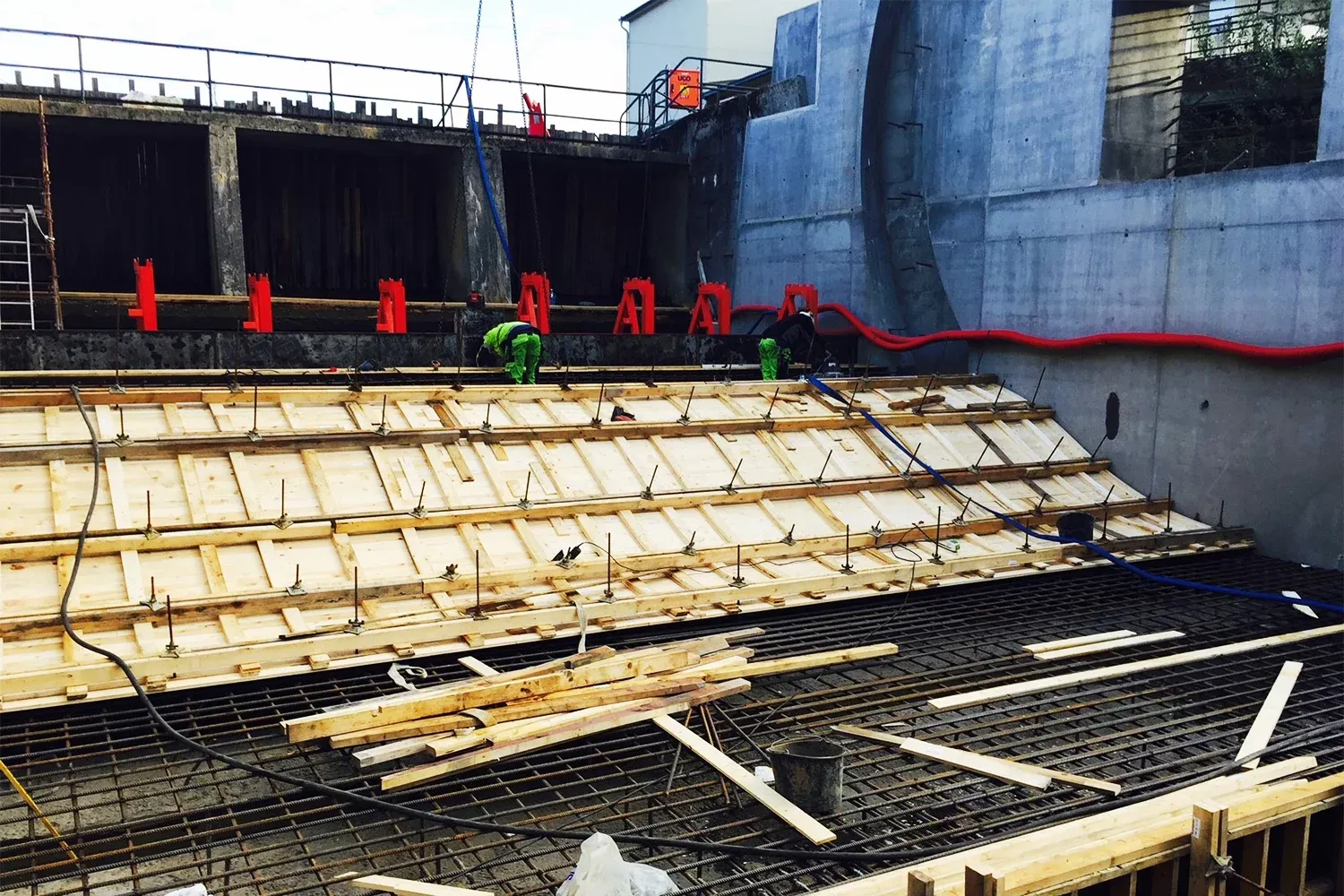 To arbeidere jobber med skråstilt forskaling i betongkanal, omgitt av armeringsjern og byggeteknisk utstyr.