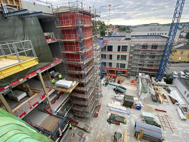 Byggeplass i bymiljø med stillas, kran og arbeidere i arbeid med oppføring av fleretasjes bygg.