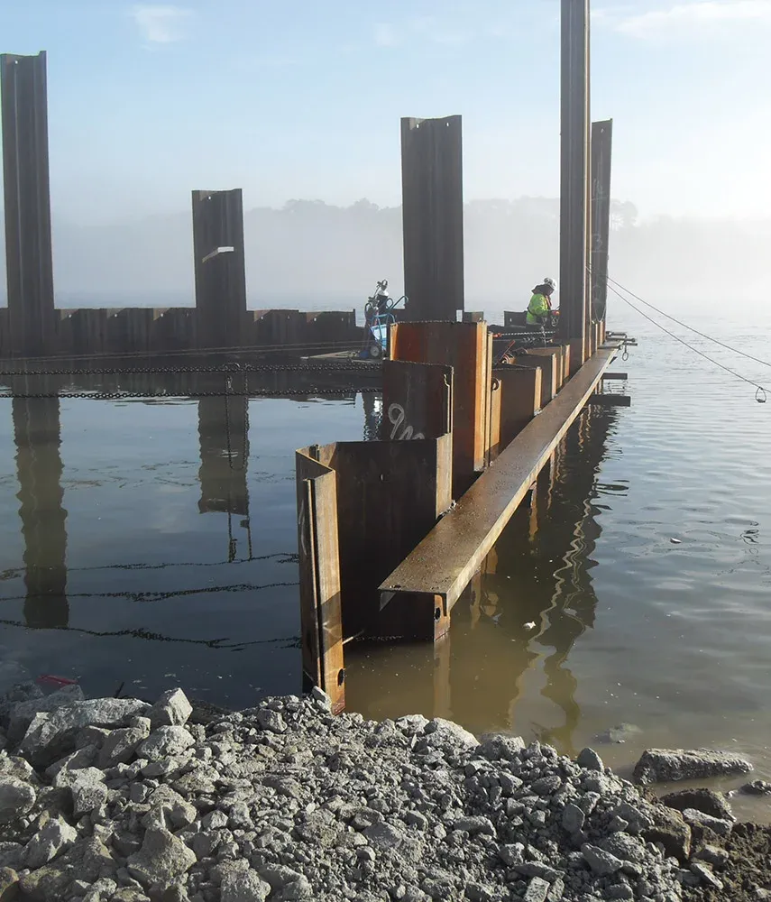 Stålspunter monteres i vannet med arbeidere til stede, som del av kai- eller vannkonstruksjon.
