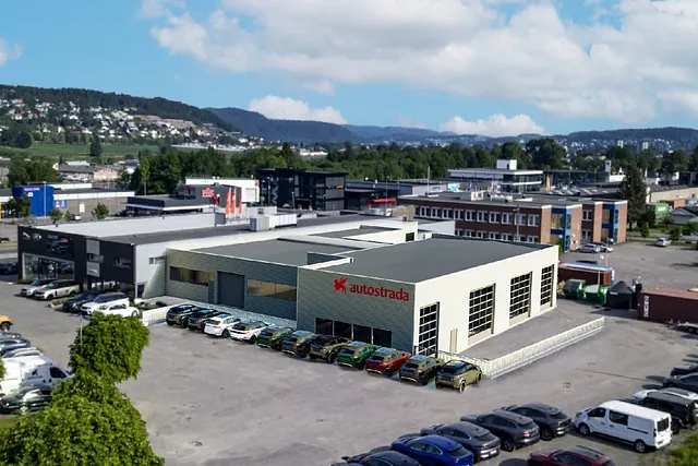 Illustrasjon av Autostrada-bygg med parkering og bilforretninger rundt, sett i urbant næringsområde.