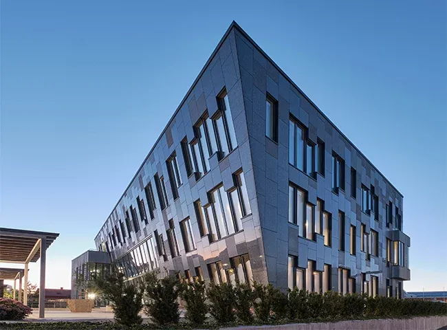 Moderne kontorbygg med mørk fasade og asymmetriske vinduer, fotografert i kveldslys.
