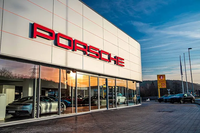 Nærbilde av Porsche-byggets fasade med stor rød logo og utstilte biler synlige gjennom glassvinduer.