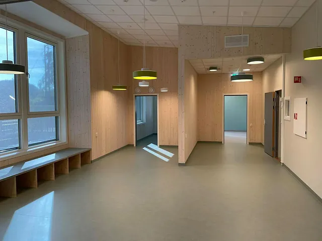 Romslig og lyst oppholdsrom med store vinduer, trepanel på veggene og moderne hengelamper.