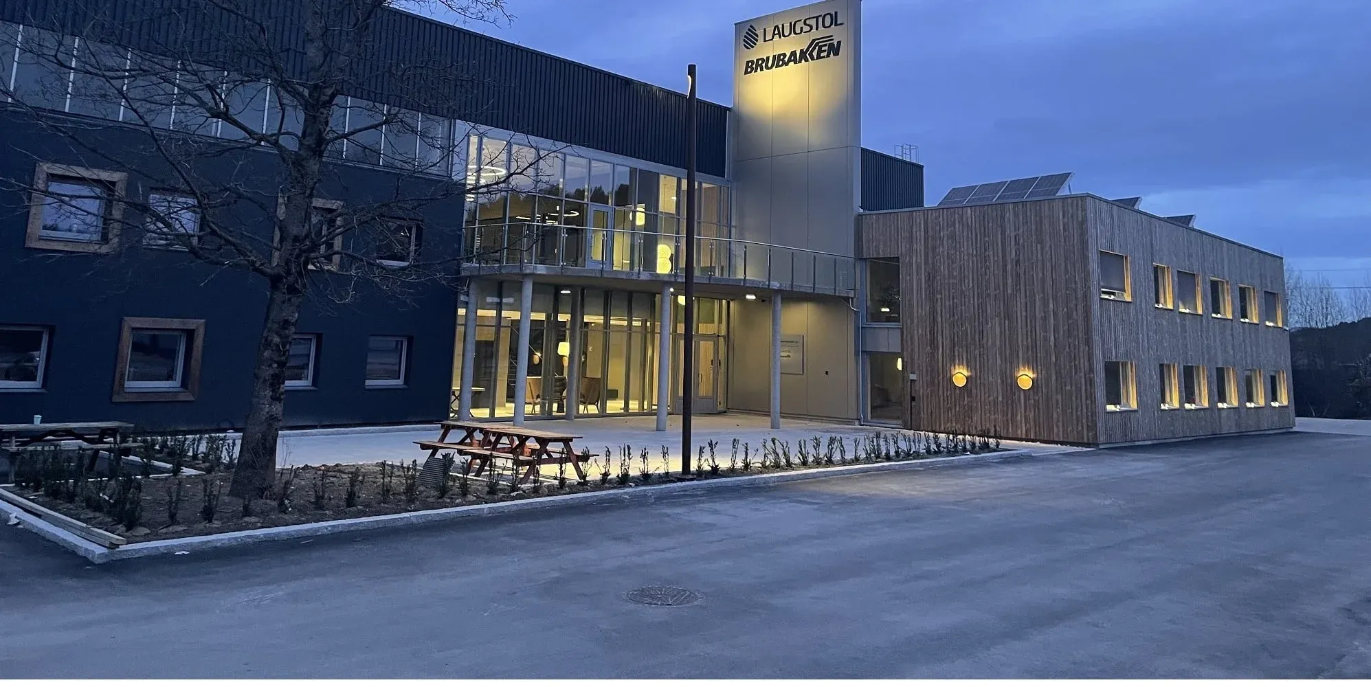 Kontorbygg med kombinasjon av treverk og mørk fasade, opplyst inngang og skilt for Laugstol og Brubakken.
