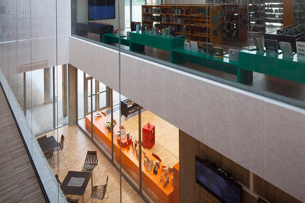 Moderne bibliotek med åpne etasjer, store glassflater og fargerike møbler i flere nivåer.