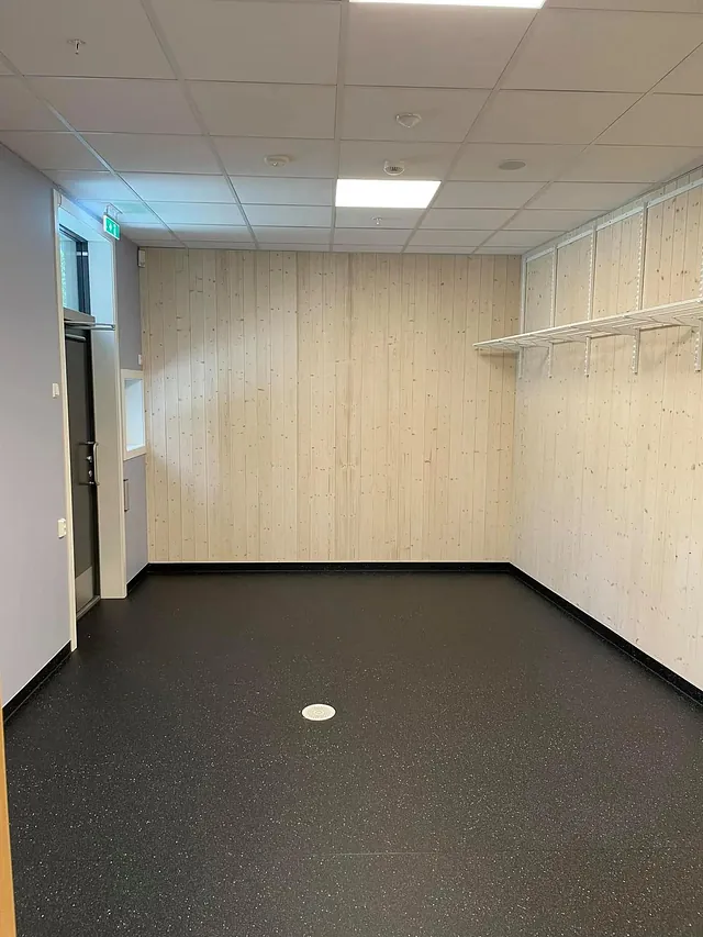 Lite rom med mørkt gulv, trepanel på veggene og hyllesystem montert langs den ene veggen.