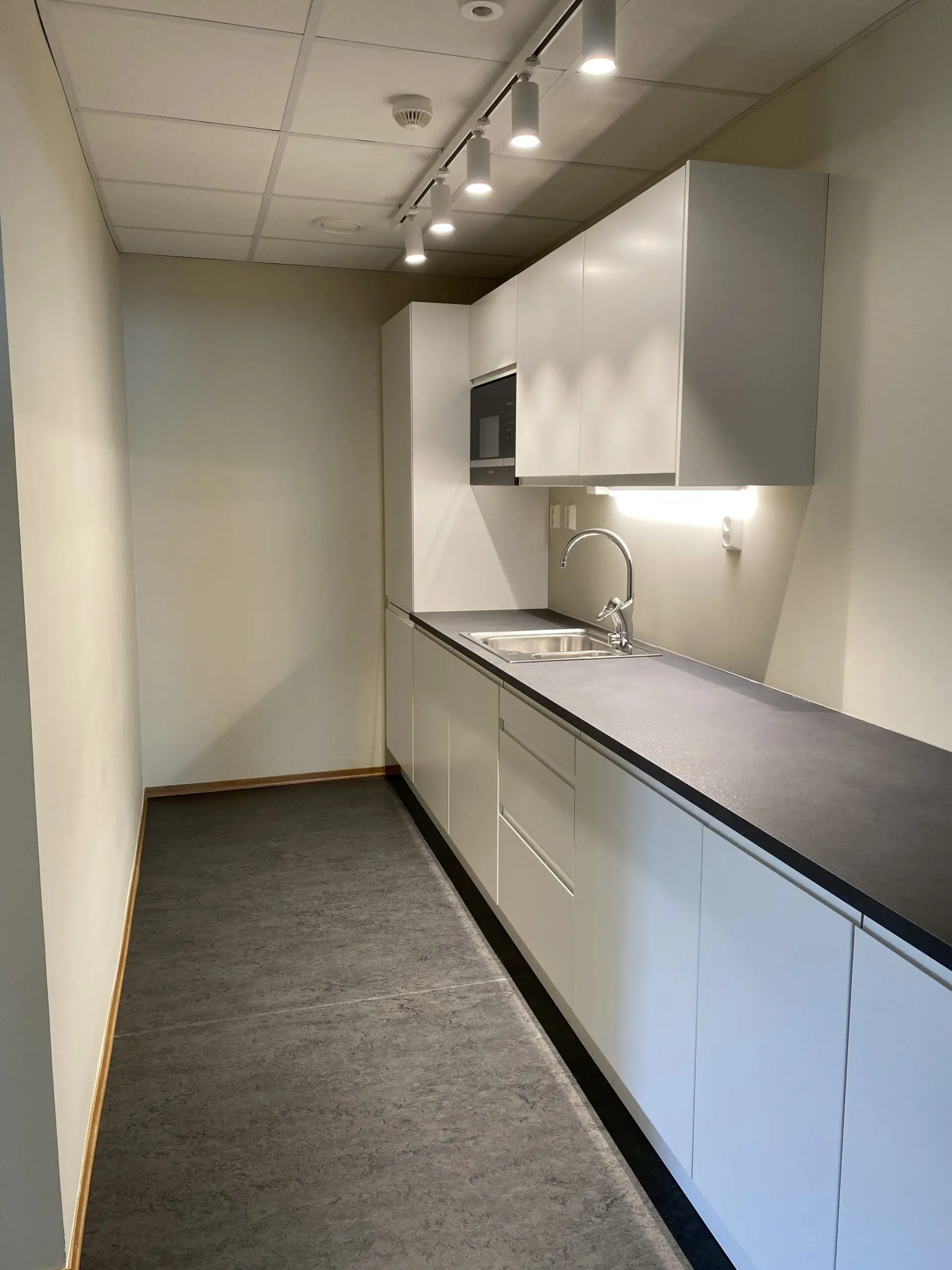 Smalt kjøkken med hvite skapdører og svart benkeplate