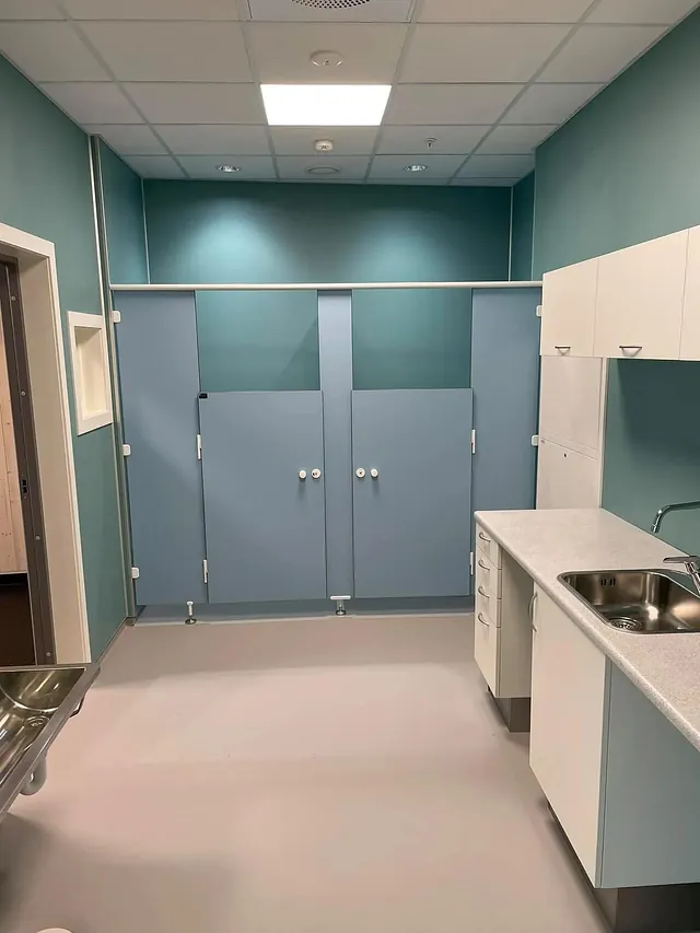 Toalettrom med blå dører til båser, servant, skap og benkeplass, i lyse og rene farger.