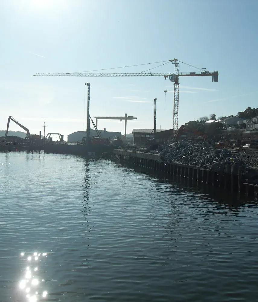 Oversiktsbilde av anleggsarbeid ved havn med flere kraner og maskiner i drift langs kaikant.