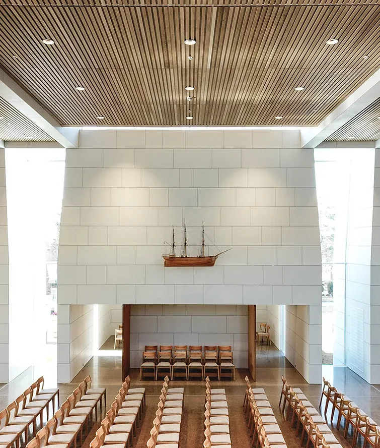 Kirkerom med lyse vegger og trekledning i taket, modellskip henger over åpning til sidesal.