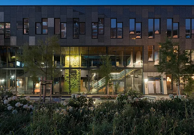 Glassfasade på Lundhs-bygget viser interiør med levende grønn vegg og belysning.