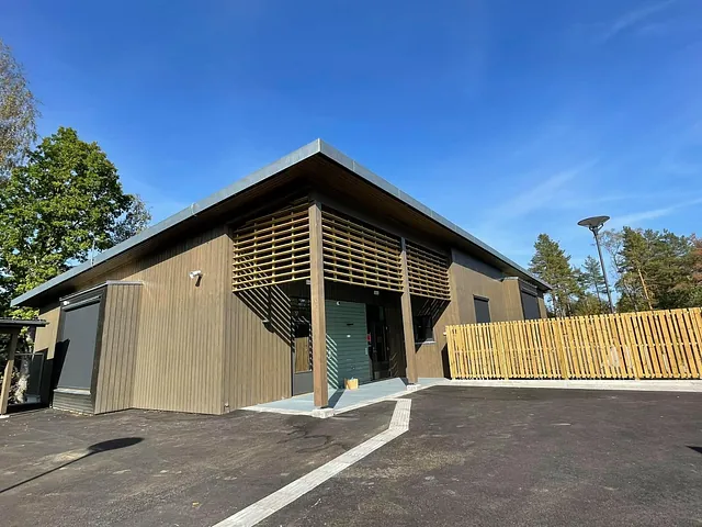 Moderne barnehagebygg i treverk med overbygg, høyt tak og inngjerdet uteområde.