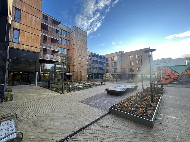Åpent gårdsrom med benker, kunstverk, gatekunst og nye bygninger med moderne fasader i tre og puss.