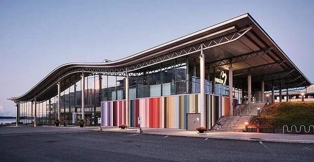 Oversiktsbilde av bygning med buet tak og glassfasade, dekorert med fargerike veggpaneler.