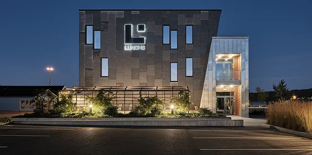 Frontfasade av Lundhs-bygget med logo, smale vinduer og pergola omgitt av grønne vekster.