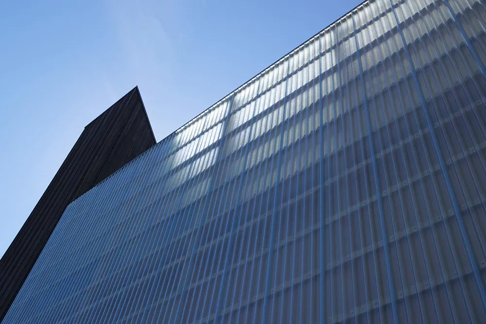 Fasade med lysgjennomsiktige plater sett nedenfra, i kontrast mot blå himmel.