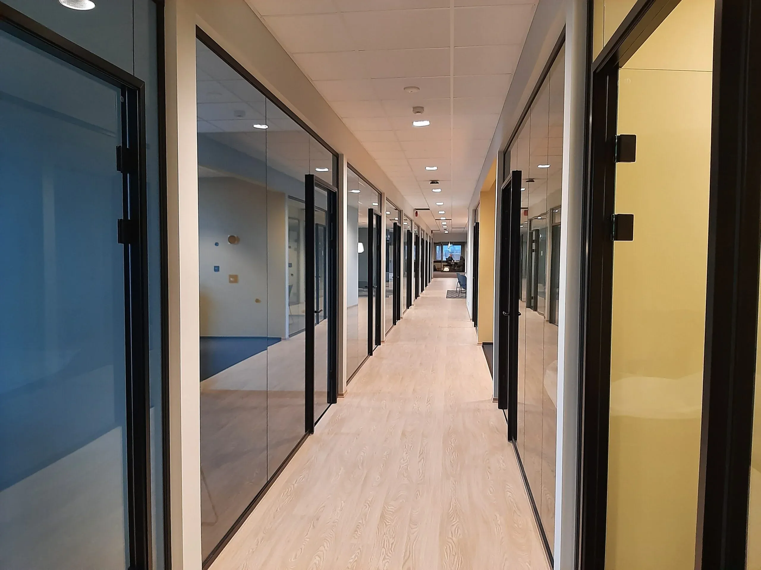 Lang kontorkorridor med glassfronter og dører til cellekontorer på begge sider.