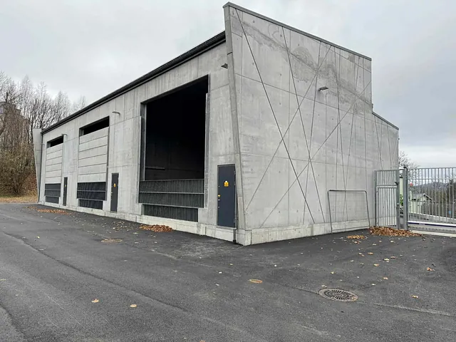 Ferdig betongbygg med store åpninger og skrå veggdetaljer, omgitt av asfalt og gjerde.