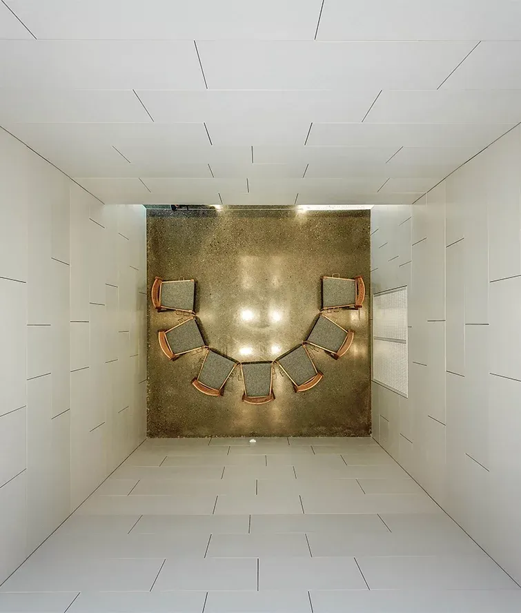 Rom sett ovenfra med stoler i halvsirkel, omgitt av lyse vegger og blankpolert betonggulv.