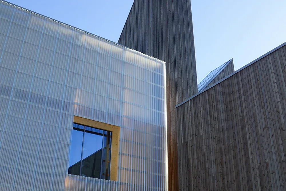 Bygningskompleks med kombinasjon av trekledning og gjennomskinnelige veggplater, og kvadratisk vindu.