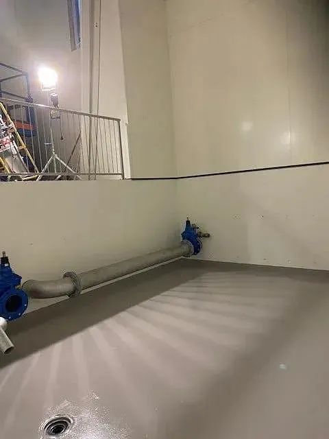 Innendørs rørgate med blå ventiler og lyse vegger, sett fra teknisk anlegg.