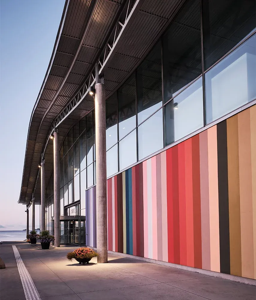 Fasade med store vinduer og fargerike vertikale striper ved inngangspartiet til moderne bygg.