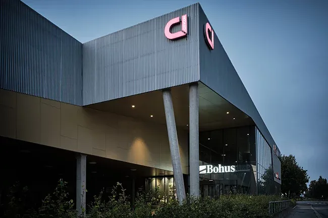 Moderne næringsbygg med Bohus-logo og store glassvinduer, sett i skumring med utvendig belysning.
