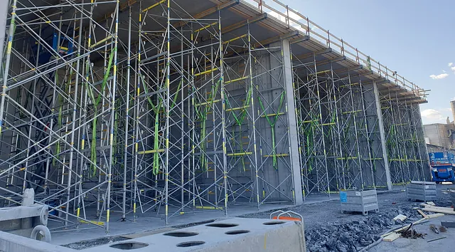 Stor betongvegg støttet av omfattende stillasstruktur under bygging på anleggsområde.