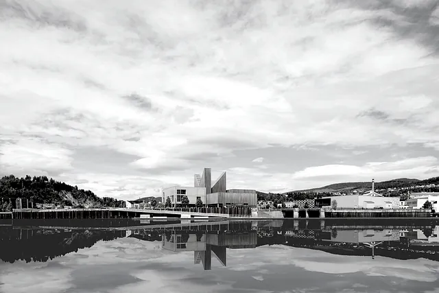 Panoramabilde av bibliotek ved elv, med karakteristiske takformer og speilbilde i vannet.