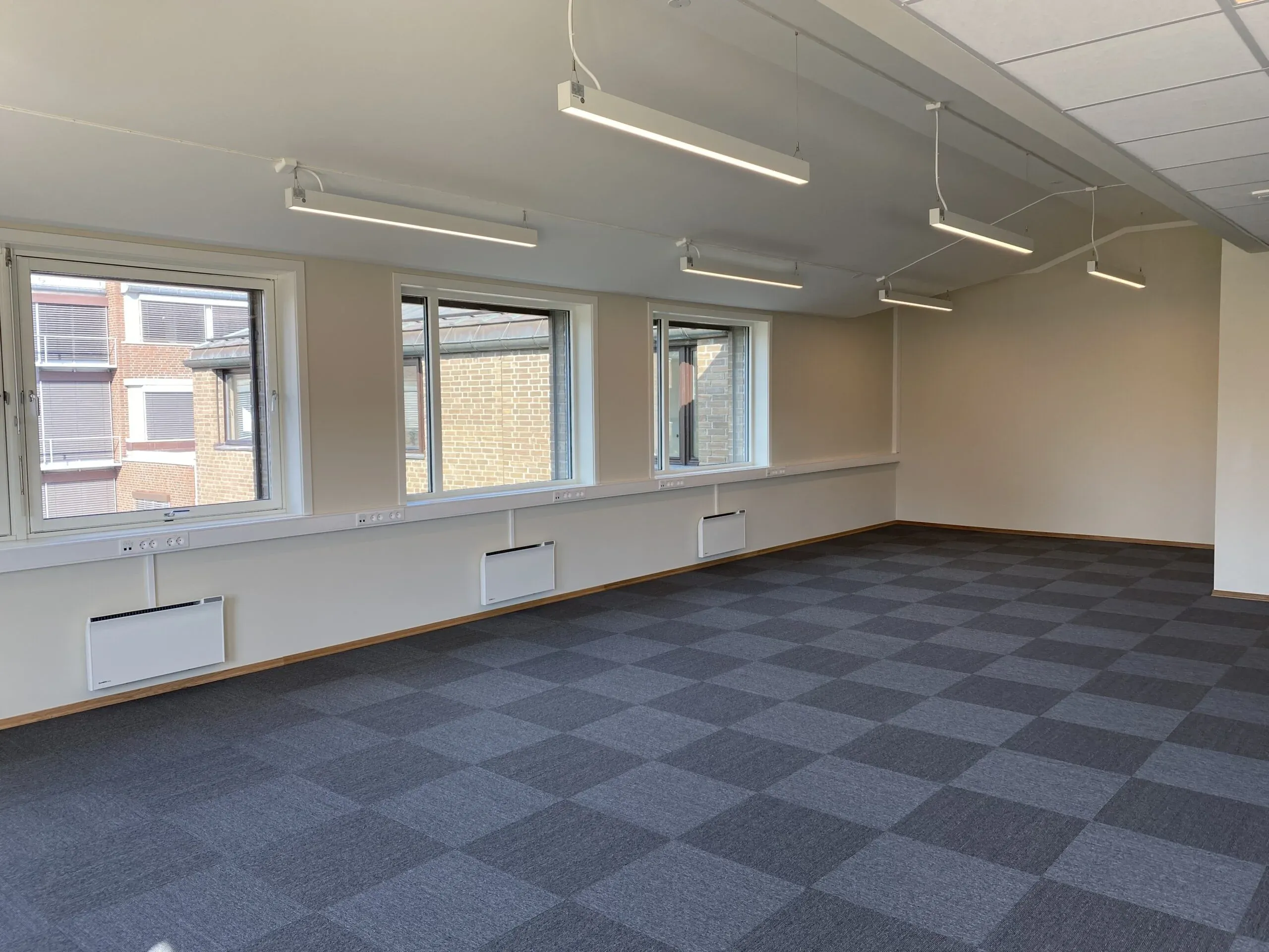 Tomt åpent kontorlokale med taklamper og oanelovner under vindu