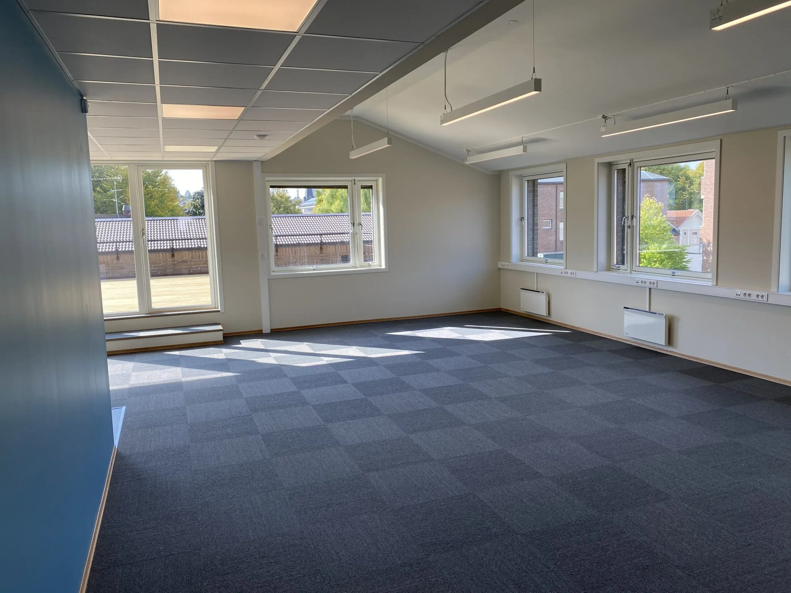 Stort tomt kontorlandskap med blått gulvteppe og hvite vegger