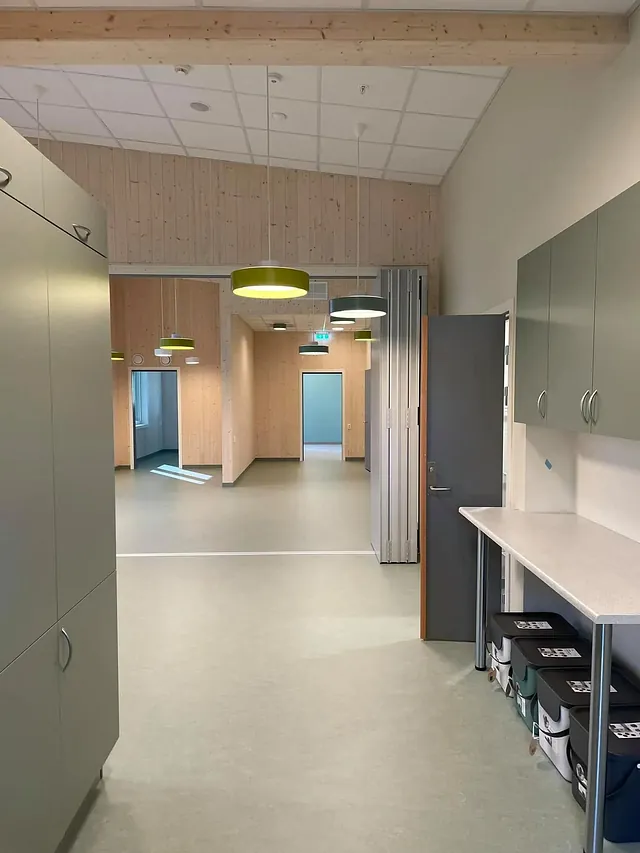 Kjøkkenkrok med oppbevaringsskap, benk og utsikt mot åpent oppholdsrom med lysegrønt gulv.