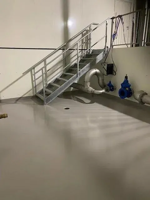 Teknisk rom med metalltrapp, rørinstallasjoner og glatt gulv med sluk i midten.