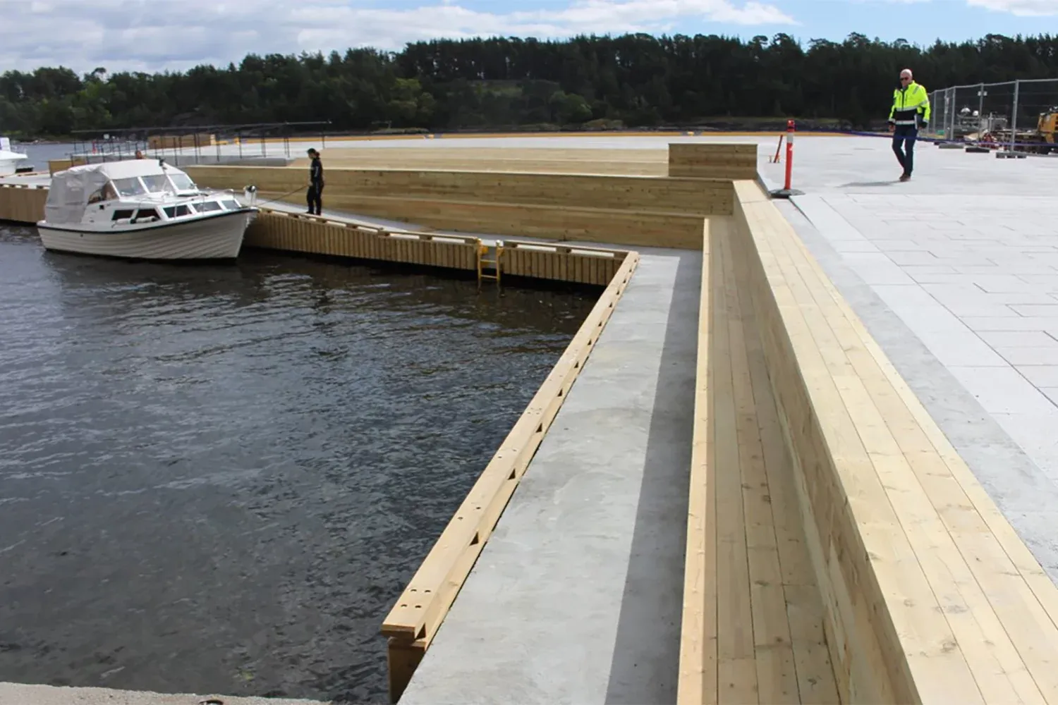 Nybygd kai med treverk og betong, der en fritidsbåt ligger fortøyd og personer inspiserer området.