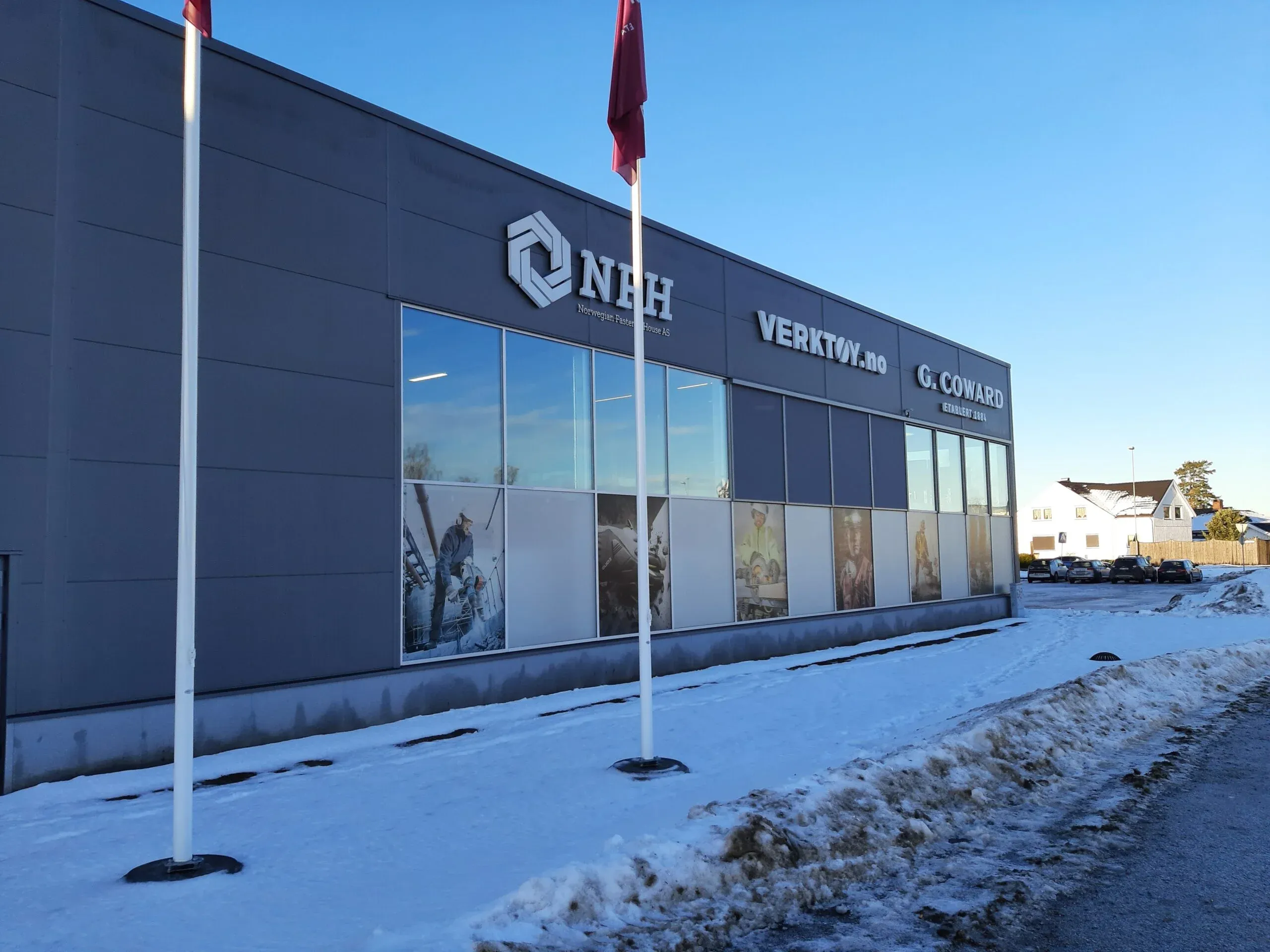 Fasade med skilt for NHF, VERKTØY.no og G. Coward, store vinduer med bilder og snø foran bygget.