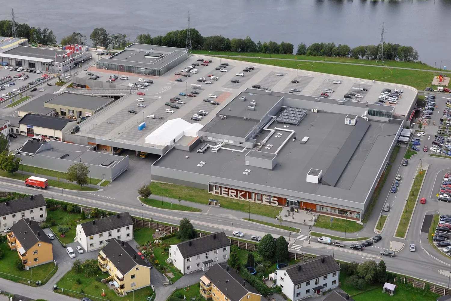 Oversiktsbilde av Herkules kjøpesenter ved elven, med tydelig logo og stor parkeringsplass.