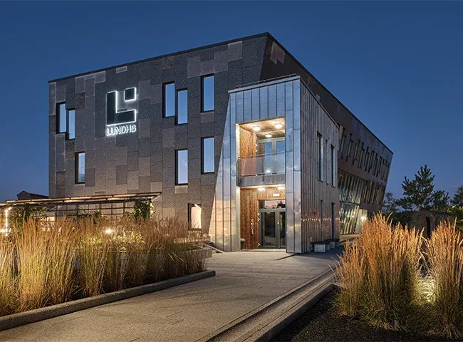 Hovedinngang til Lundhs-bygget med metallkledning, belysning og beplantet inngangsparti.
